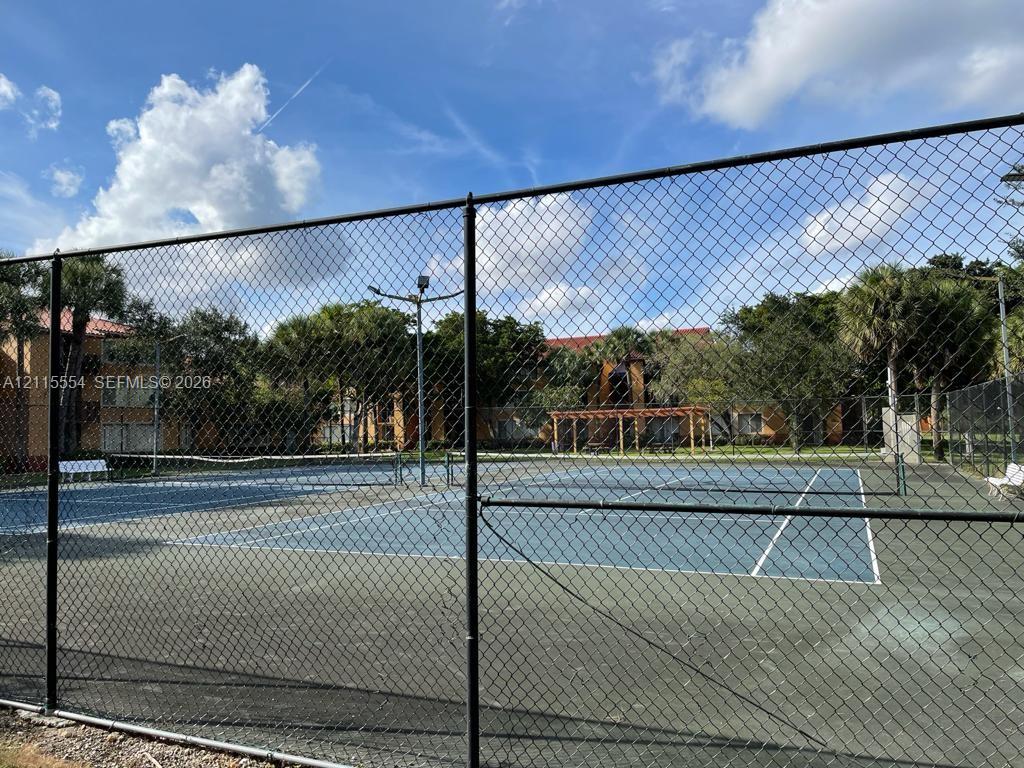 Tennis court with a blue surface, chain-link perimeter fencing, and pole-mounted lighting