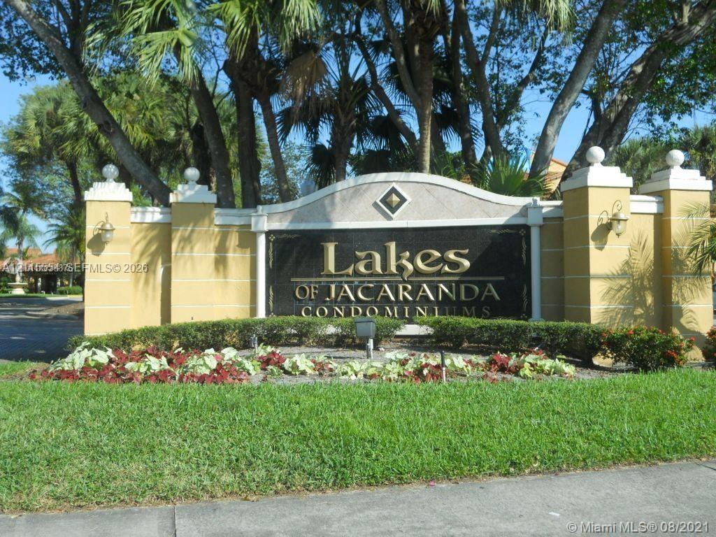 Stucco community entrance monument featuring decorative finials, wall-mounted exterior lighting, and manicured landscaping