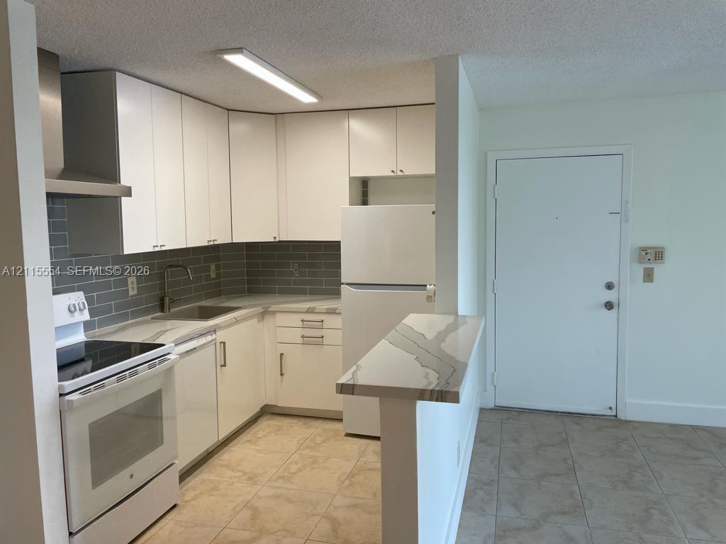 Kitchen featuring white cabinetry, quartz countertops with a waterfall edge, subway tile backsplash, stainless steel range hood, and tile flooring