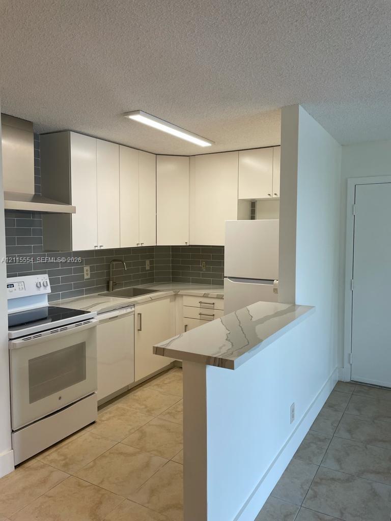 Kitchen featuring white flat-panel cabinetry, a stone-patterned breakfast bar, gray subway tile backsplash, and tile flooring