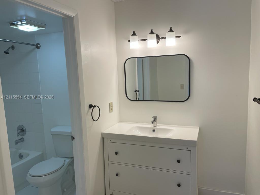 Bathroom featuring a vanity with a rectangular sink, a rounded rectangular wall mirror with a black frame, a three-light fixture with frosted glass shades, and a shower-tub combination