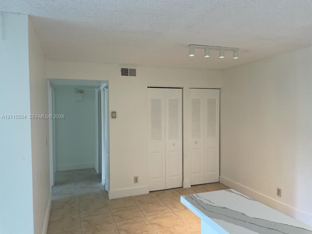 Interior space featuring tile flooring, dual white louvered closet doors, and a linear track lighting fixture