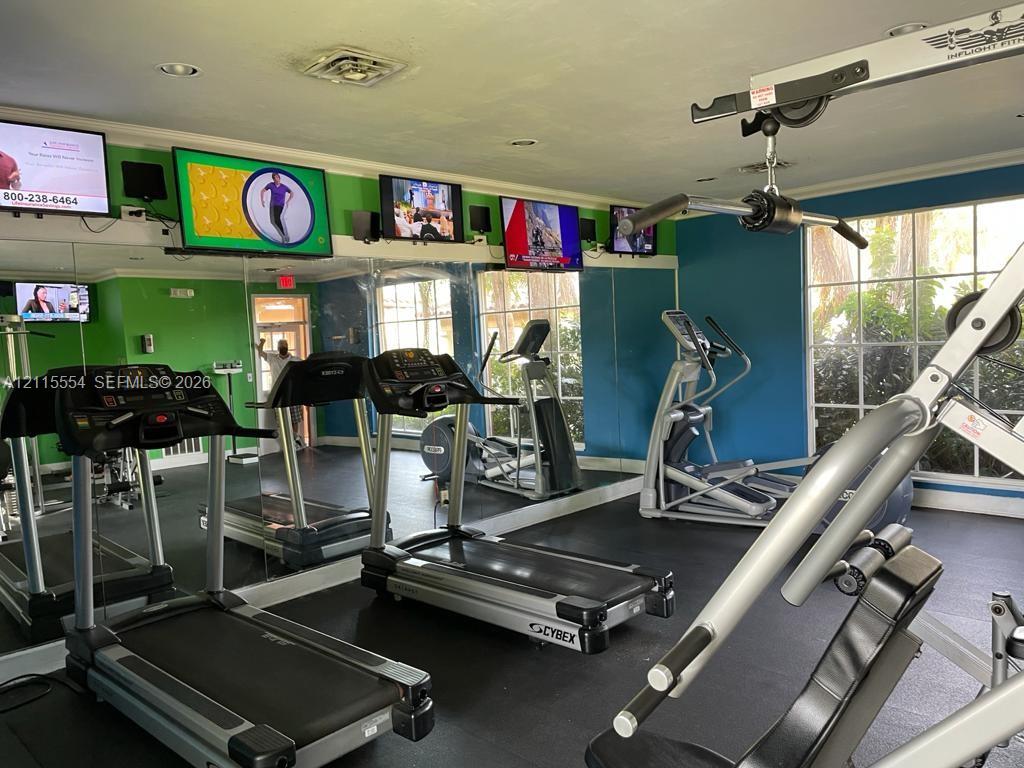 Fitness room featuring mirrored walls, rubberized flooring, and multiple wall-mounted television displays