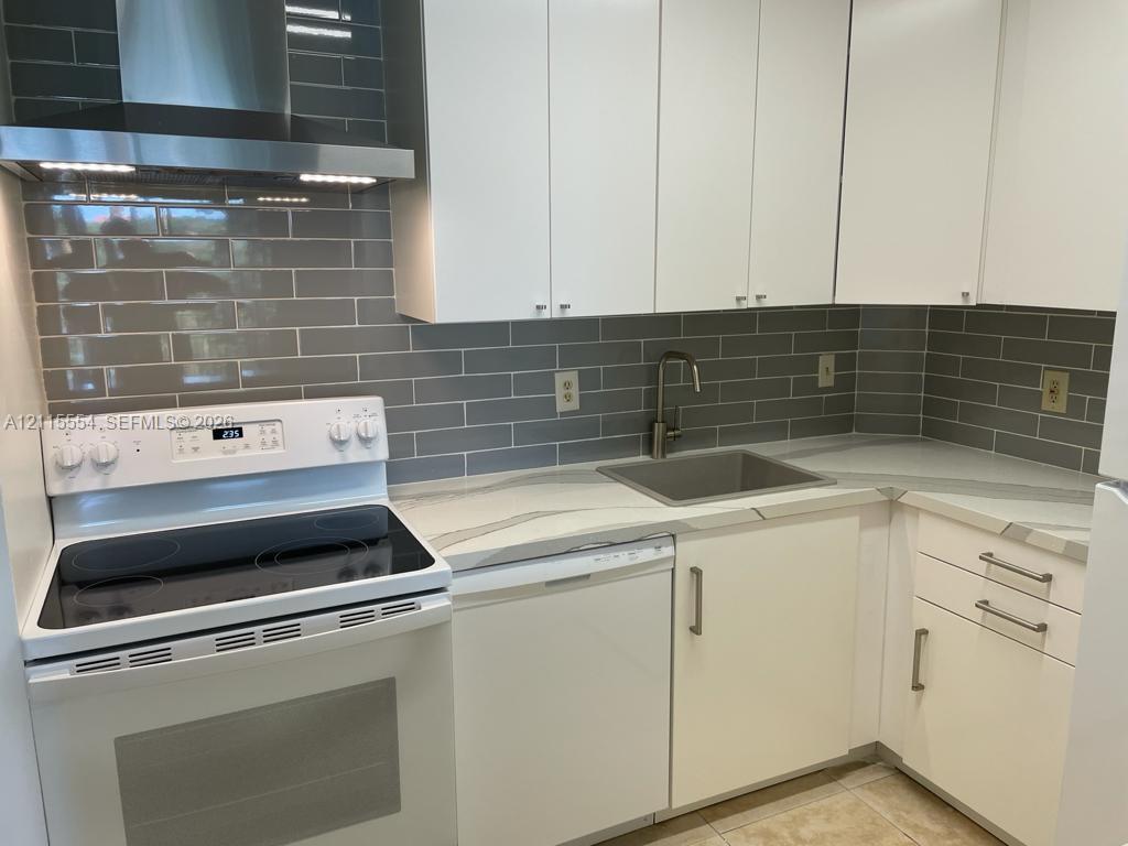 Kitchen featuring white cabinetry, solid-surface countertops with grey veining, subway tile backsplash, stainless steel range hood, and integrated sink with gooseneck faucet