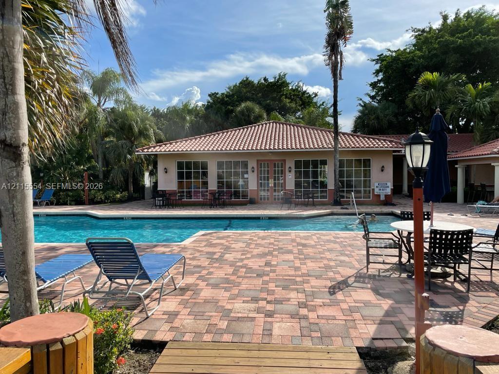 Outdoor swimming pool featuring a multi-tone paver deck, terracotta-style roof tiles, and extensive grid-pane windows
