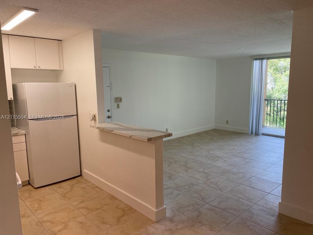 Kitchen featuring white cabinetry and a pass-through counter, tile flooring throughout, and sliding glass doors leading to a balcony