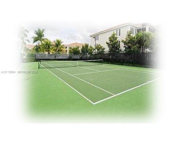 Tennis court featuring a hard surface, perimeter fencing, and surrounding mature landscaping