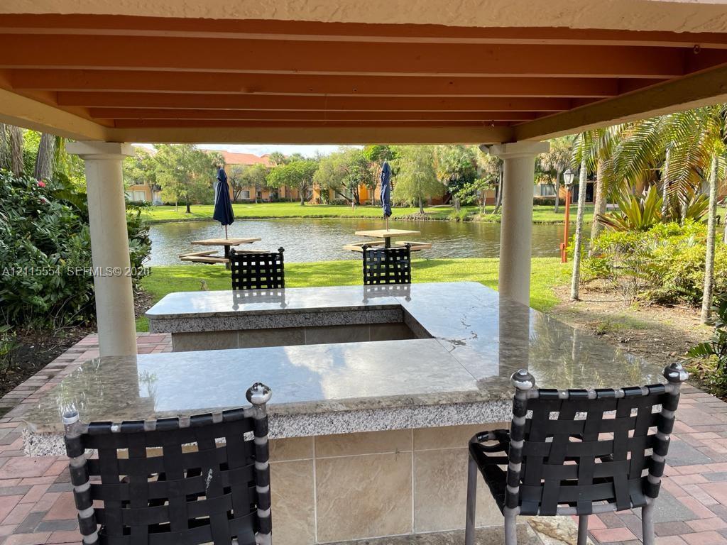 Outdoor kitchen area featuring a U-shaped stone countertop, structural pergola, and paver flooring