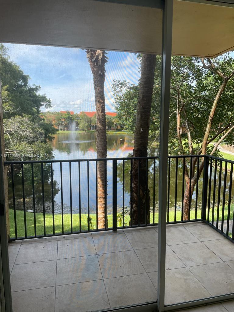 Screened balcony featuring large-format tile flooring and metal railings, overlooking a lake with a central fountain