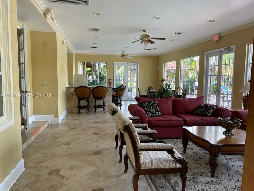 Spacious room featuring tile flooring with decorative inserts, recessed lighting, ceiling fans, multiple sets of glass-paned double doors, and a built-in bar area with a stone-finish counter