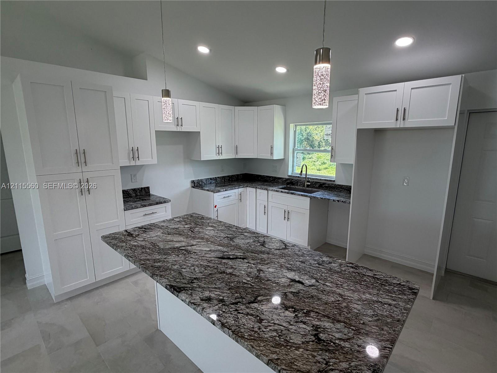 Kitchen featuring white shaker-style cabinetry, dark patterned stone countertops, a central island, recessed lighting, and dual textured glass pendant lights