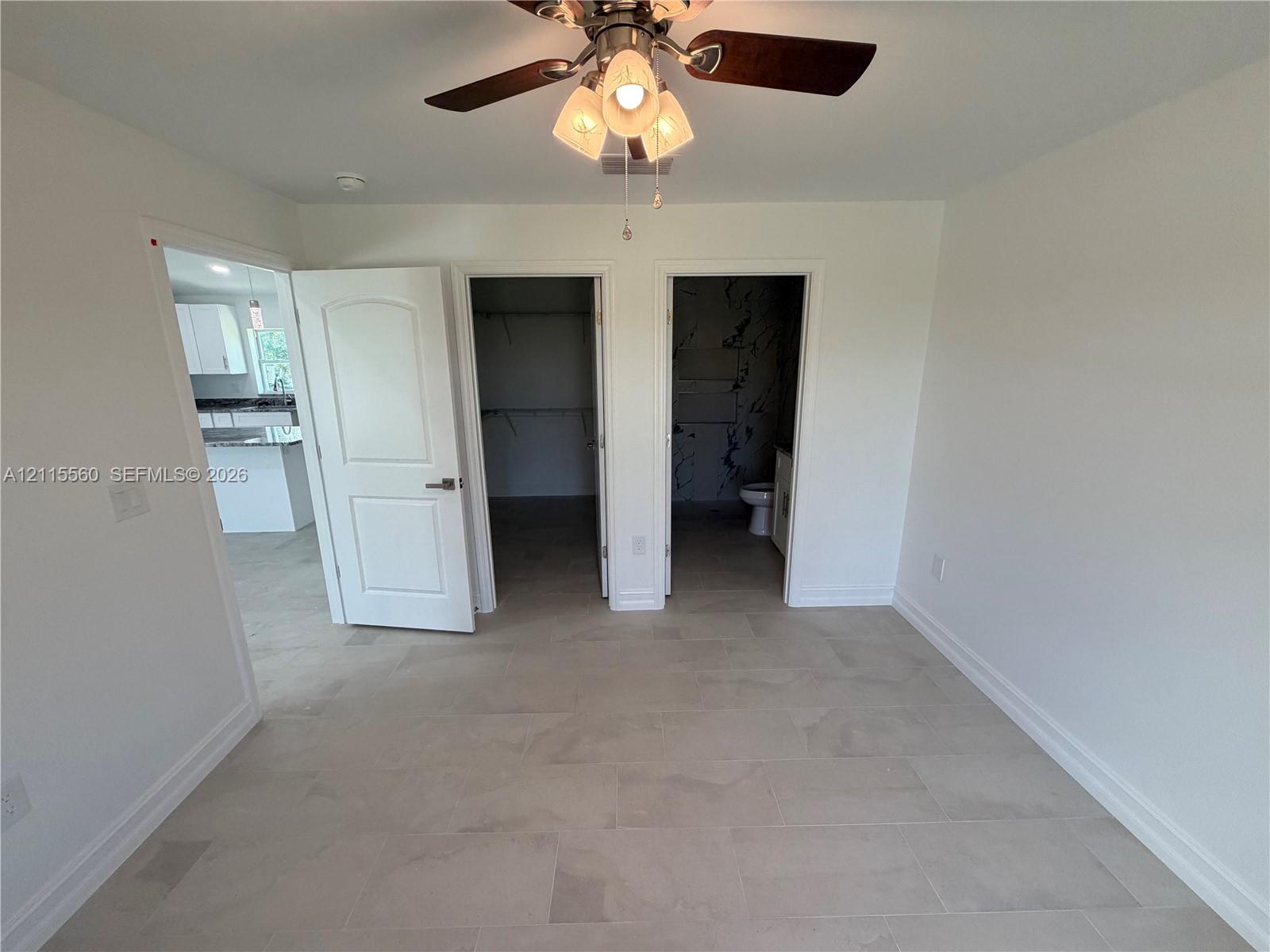 Neutral-toned tile flooring, three-panel interior door, ceiling fan with glass-shaded light fixture, and two separate interior entry points