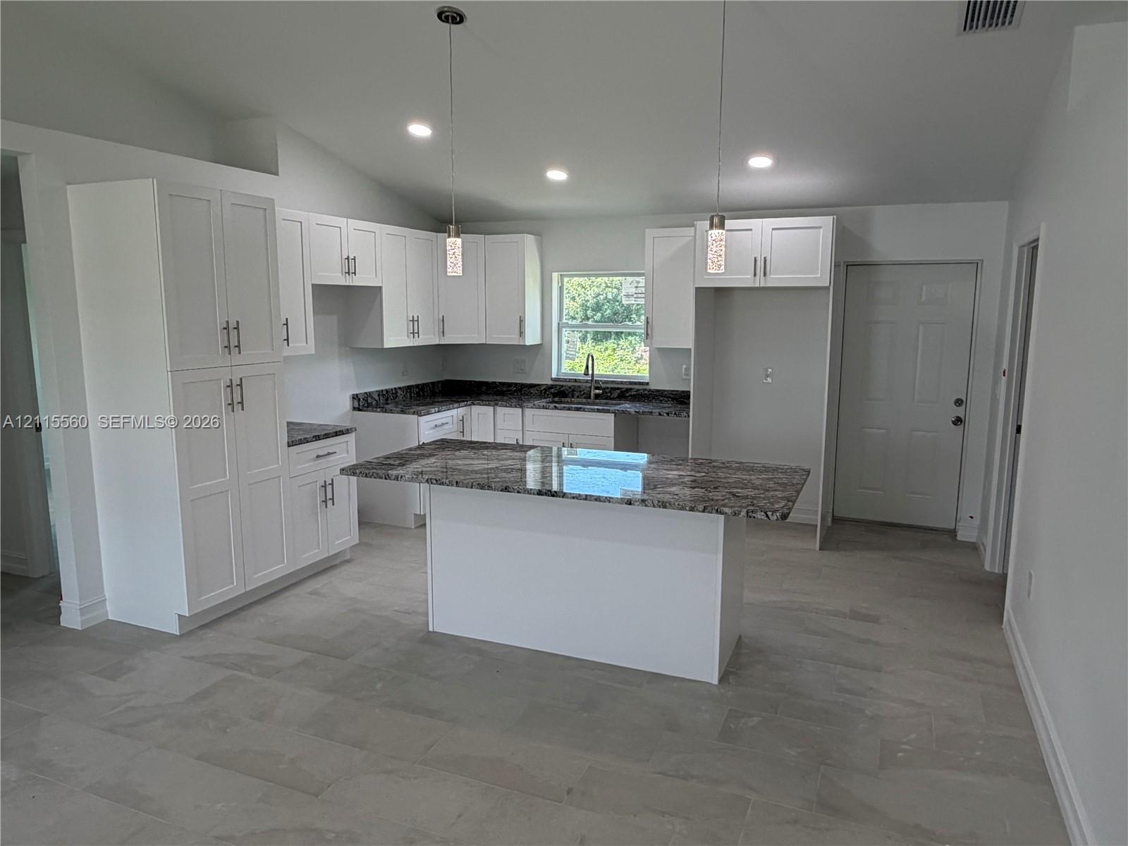 Kitchen featuring white cabinetry, patterned stone-surface countertops, central island, pendant lighting, and tile flooring