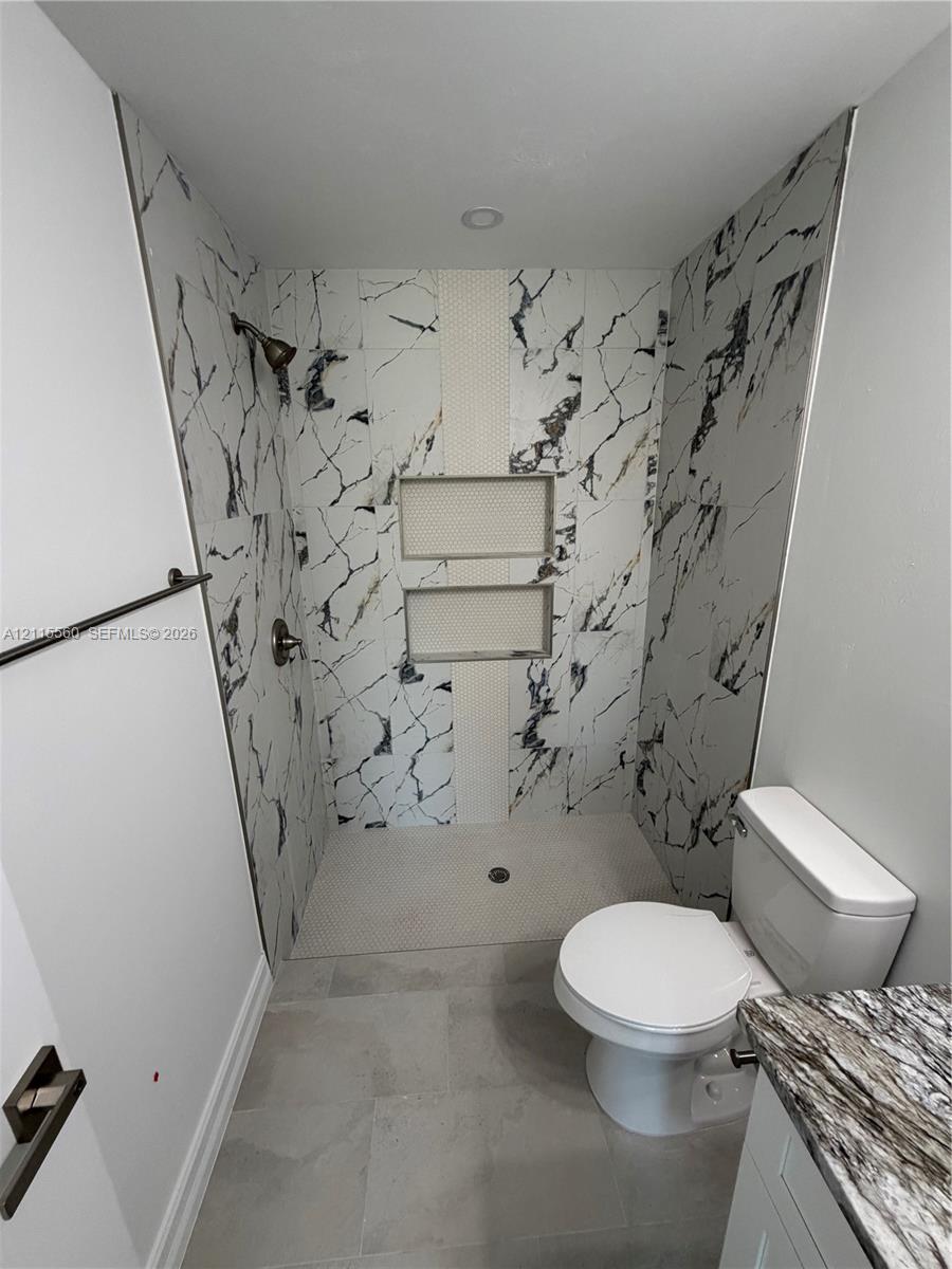 Walk-in shower with floor-to-ceiling large-format veined tile, integrated dual shelving niches, matte black shower hardware, and custom stone-finish vanity countertop