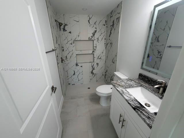 Bathroom featuring a walk-in shower with stone-patterned tile, dual built-in shower niches, vanity with a stone countertop and integrated sink, and an LED-backlit mirror