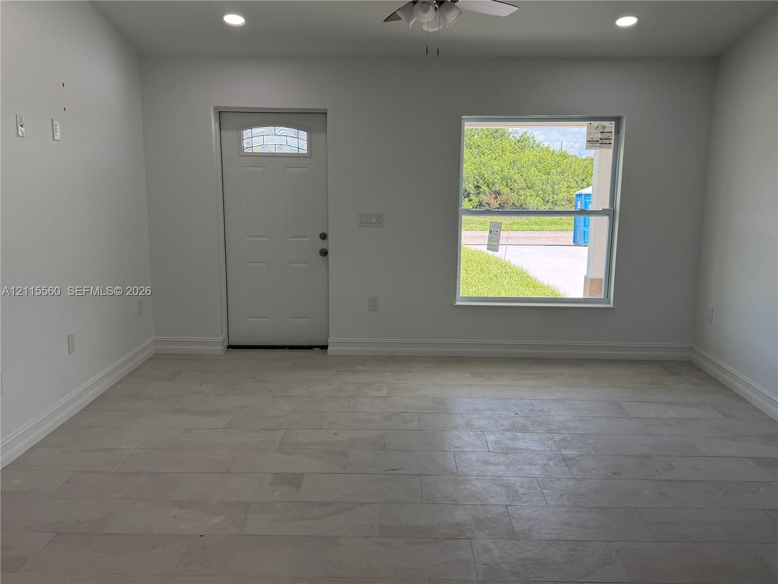Neutral-toned tile flooring, recessed ceiling lighting, ceiling fan, and white entry door with a decorative glass insert