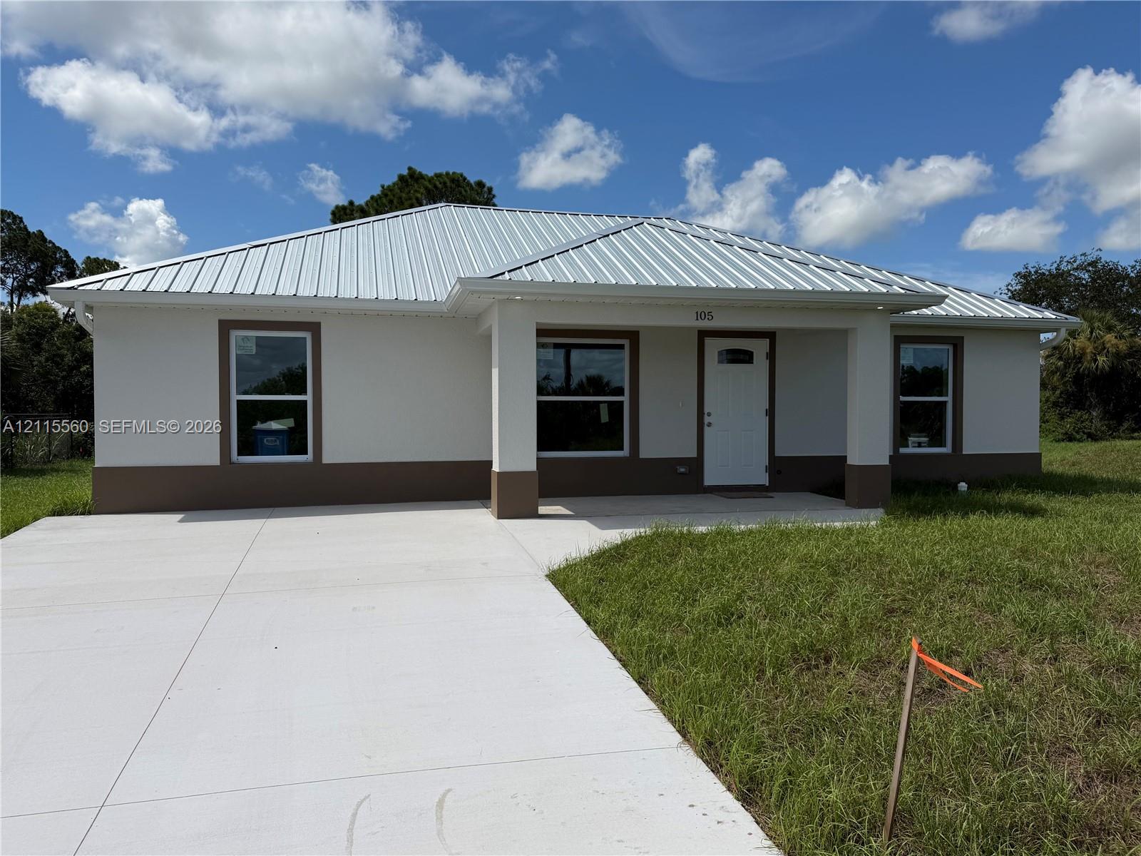 Single-story exterior featuring a metal roof, stucco finish, covered entryway, and a concrete driveway
