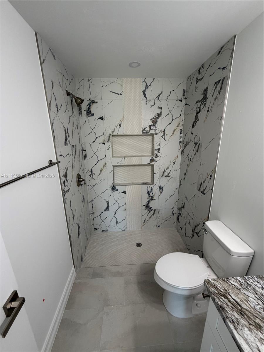 Walk-in shower featuring large-format patterned wall tile, dual recessed shelving niches, a textured stone-tiled floor, and a metal shower fixture