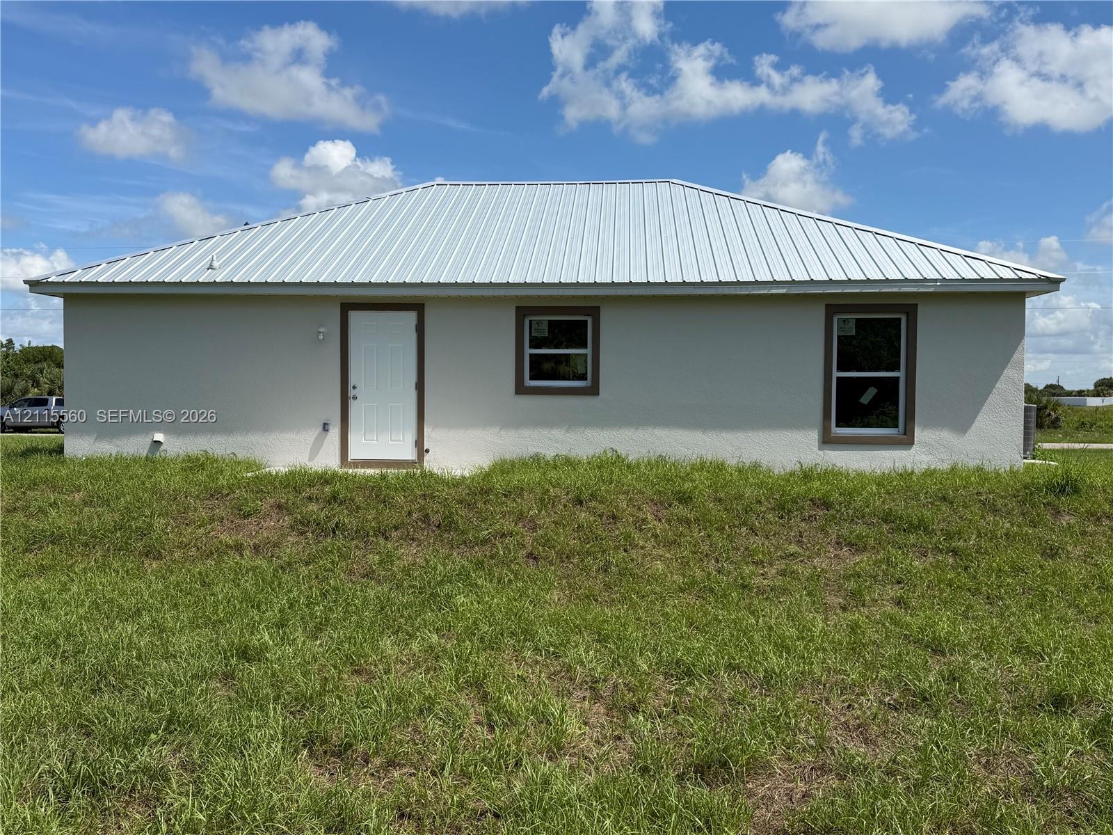 Stucco exterior featuring a metal roof, white entry door, and rectangular windows with trim