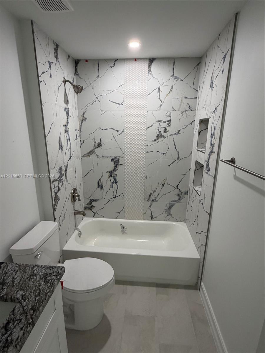 Full-height tub surround with large-format veined tile, vertical mosaic accent inlay, built-in double shower niches, recessed ceiling lighting, and stone-top vanity