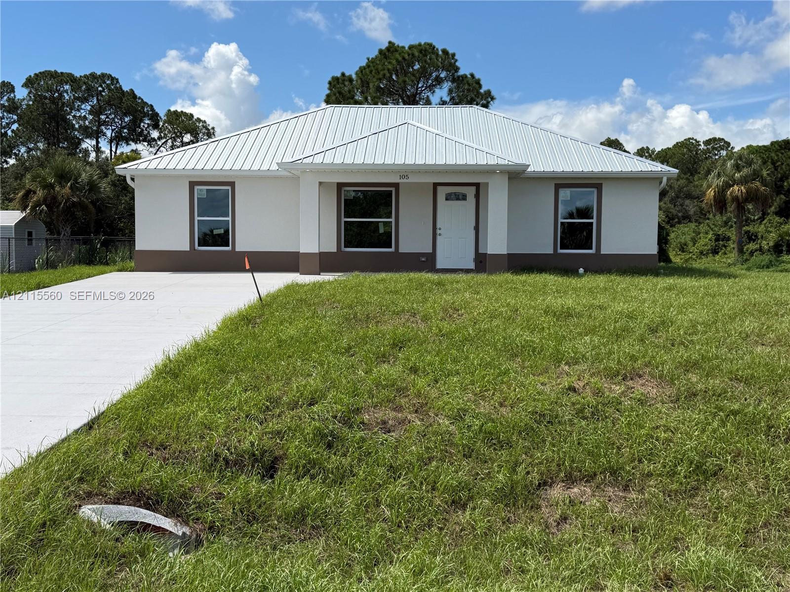 Single-story residence featuring a standing-seam metal roof, stucco exterior with a contrasting base, and a concrete driveway