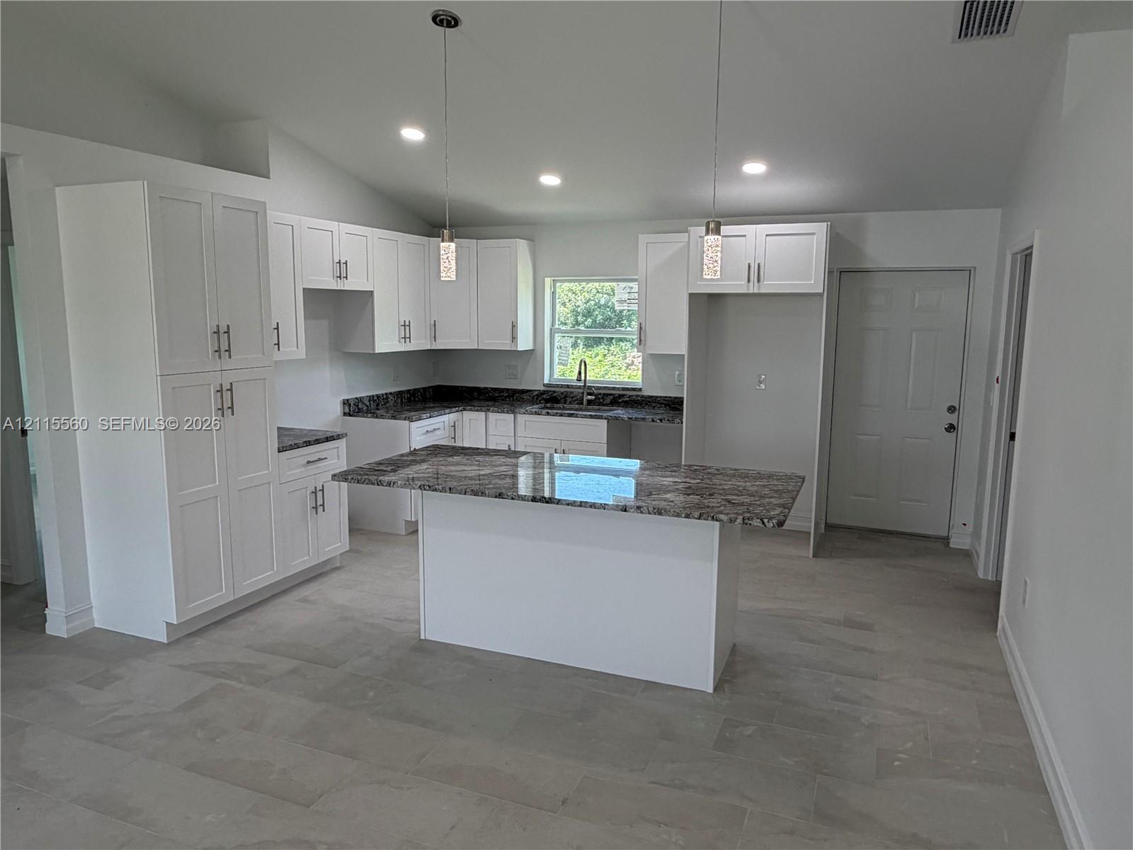 Kitchen featuring white shaker-style cabinetry, a central island with patterned stone-finish countertops, tile flooring, and dual hanging pendant lights