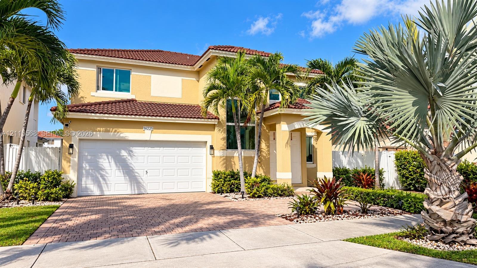 Two-story stucco exterior featuring a tiled roof, multi-car garage, and paver driveway
