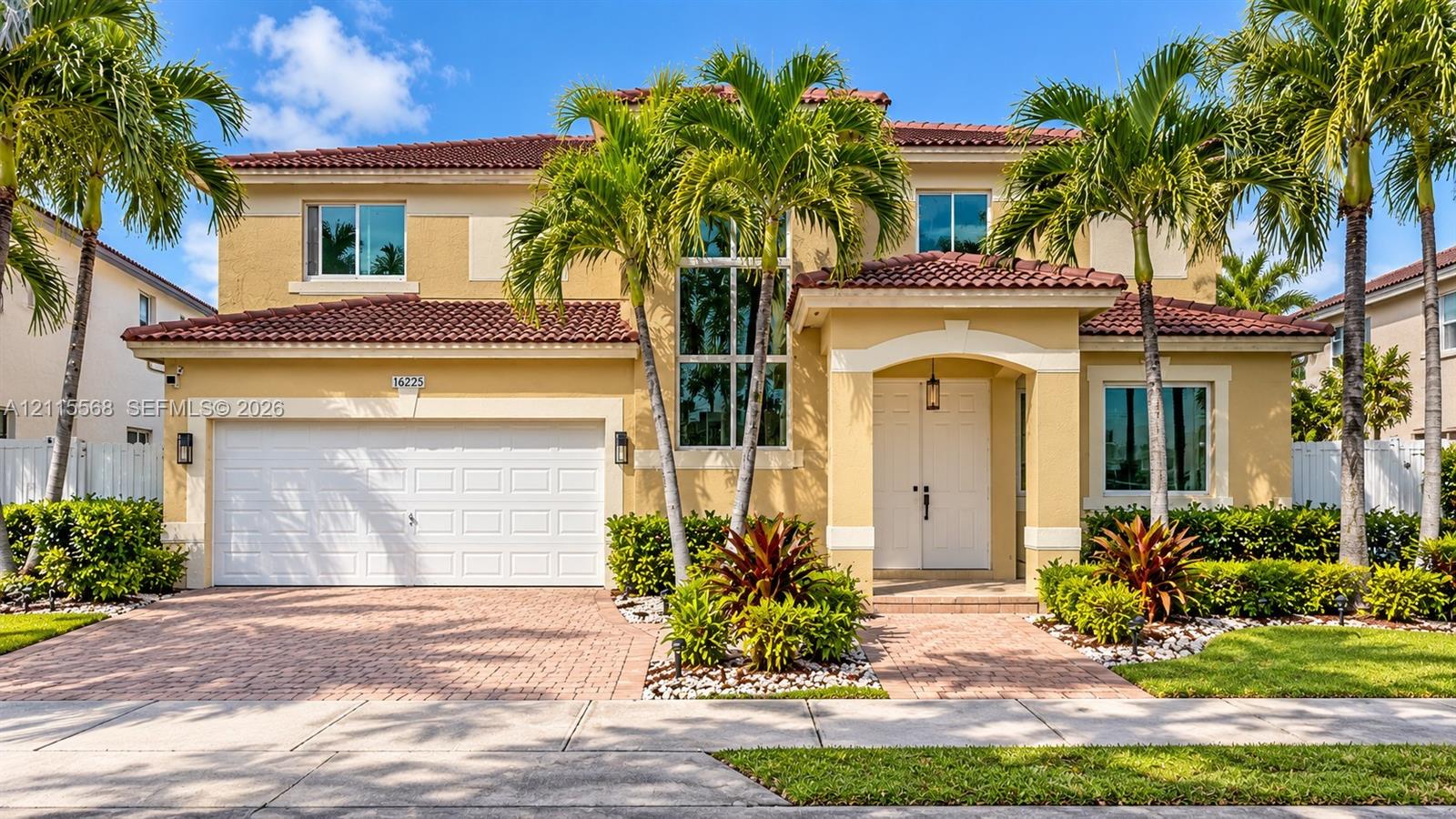Two-story residence featuring a tile roof, stucco exterior, paver driveway, double-door entryway, and floor-to-ceiling accent windows