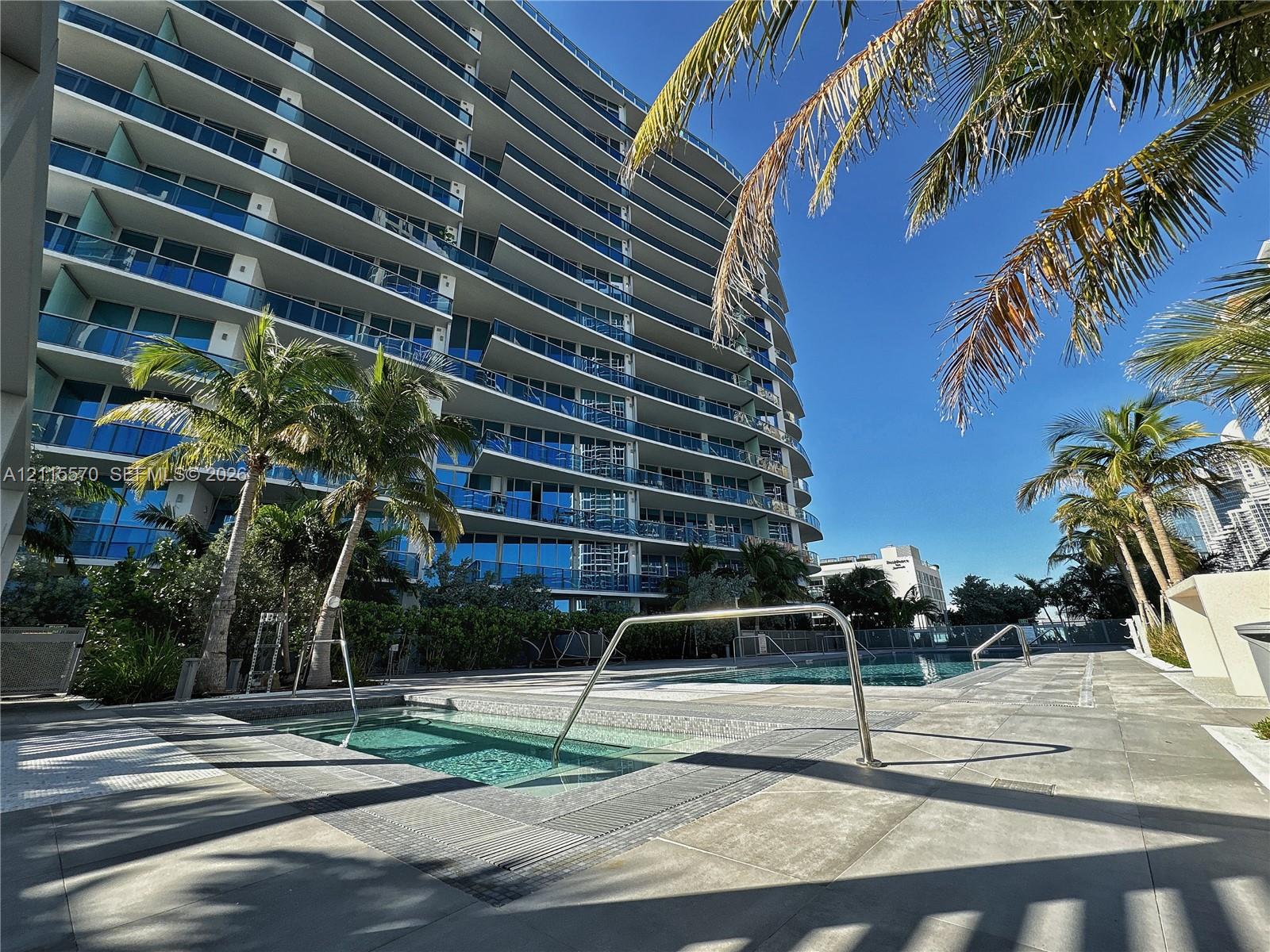 High-rise exterior with glass-railed balconies, ground-level pool, tiled deck, and built-in hot tub
