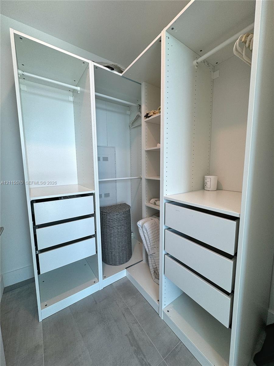 Custom reach-in closet featuring white modular cabinetry, integrated shelving, tiered drawer storage, and hanging rods