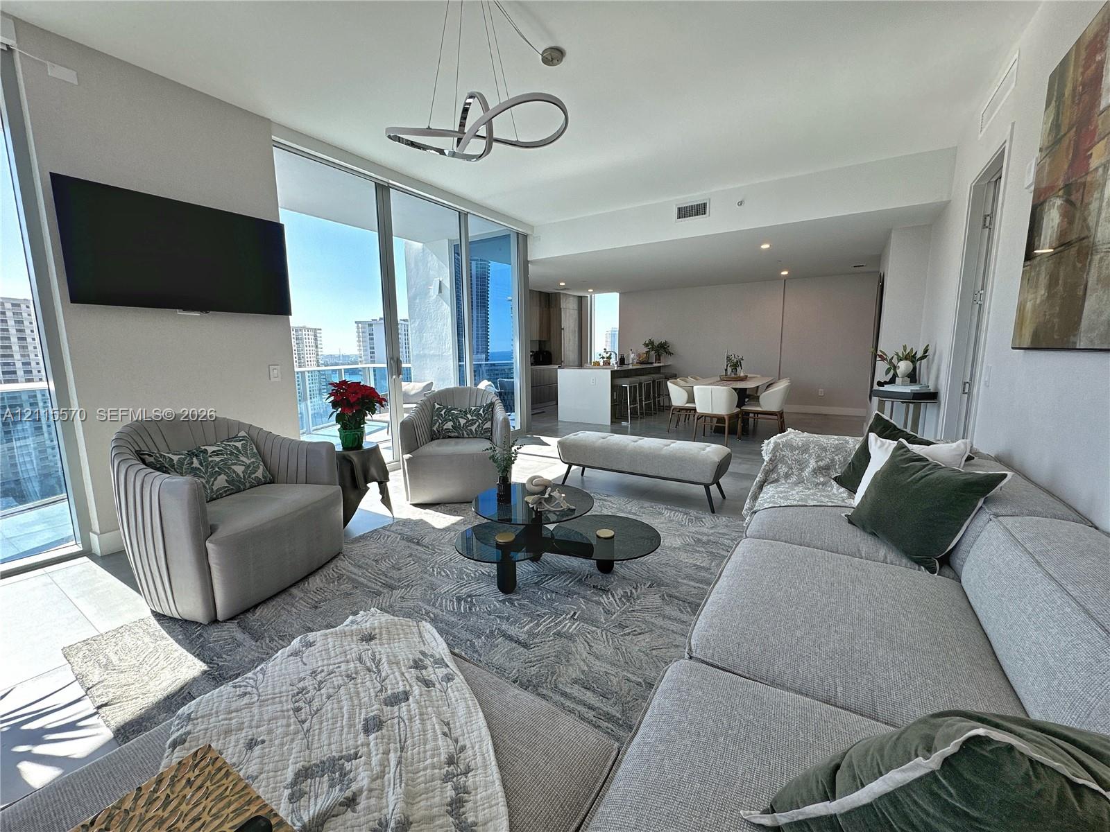 Open-concept living area featuring floor-to-ceiling glass sliding doors, recessed lighting, modern geometric chandelier, and tile flooring