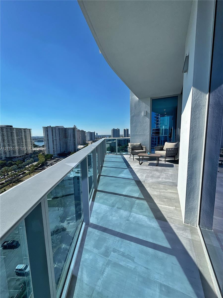 Covered private balcony featuring large-format ceramic tile flooring and a glass panel railing