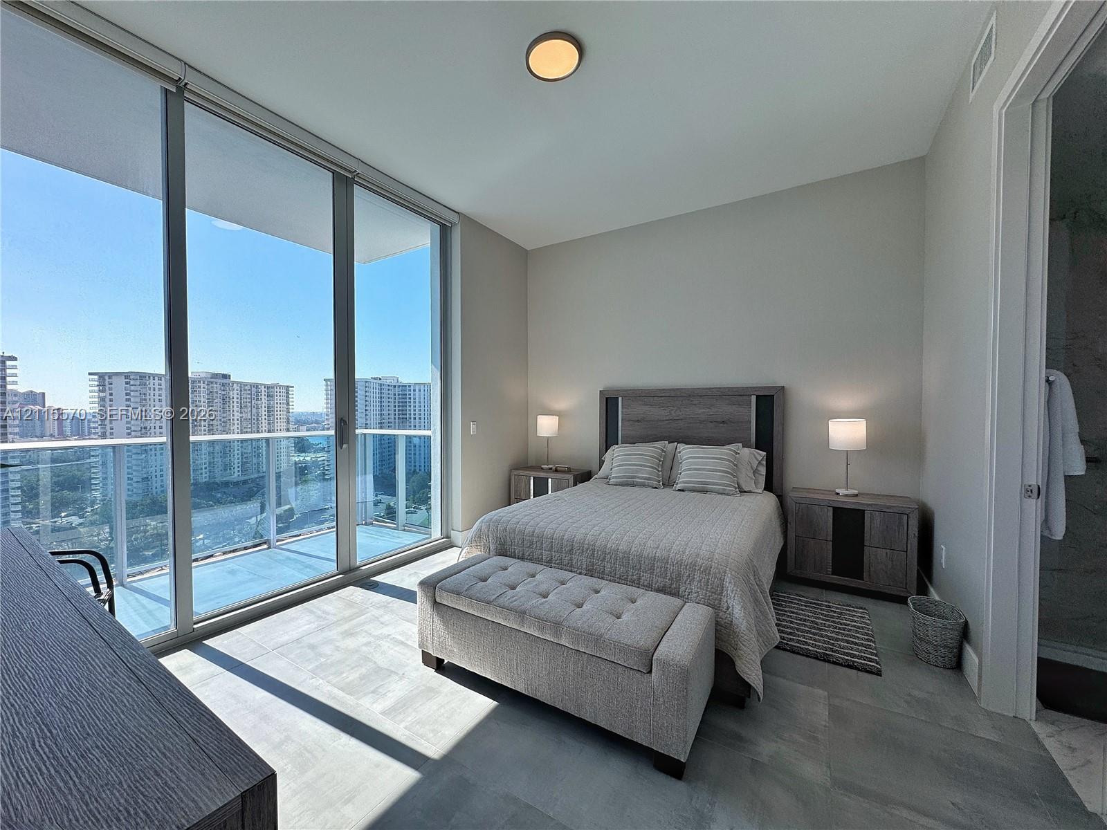 Floor-to-ceiling windows, private balcony, neutral-tone tile flooring, and flush-mount ceiling lighting