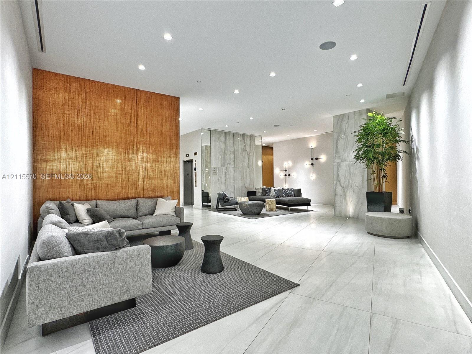 Large-format stone tile flooring, textured wood-paneled accent wall, stone-clad structural pillars, recessed ceiling lighting, and multi-arm geometric wall sconces