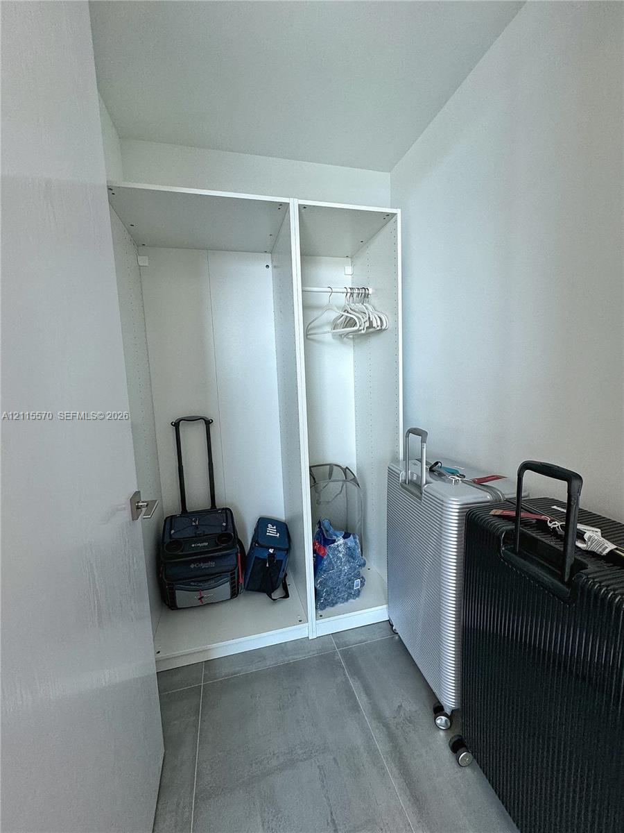Built-in white storage cabinetry featuring adjustable shelving and a hanging rod, finished with large-format grey tile flooring