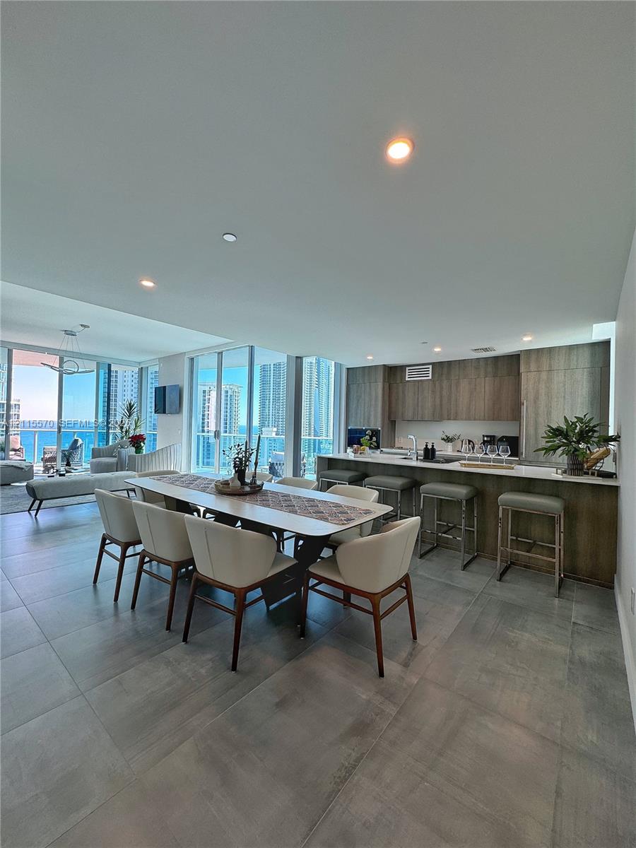 Open-concept interior featuring large-format tile flooring, flat-panel cabinetry, a kitchen island with bar seating, and expansive floor-to-ceiling glass windows