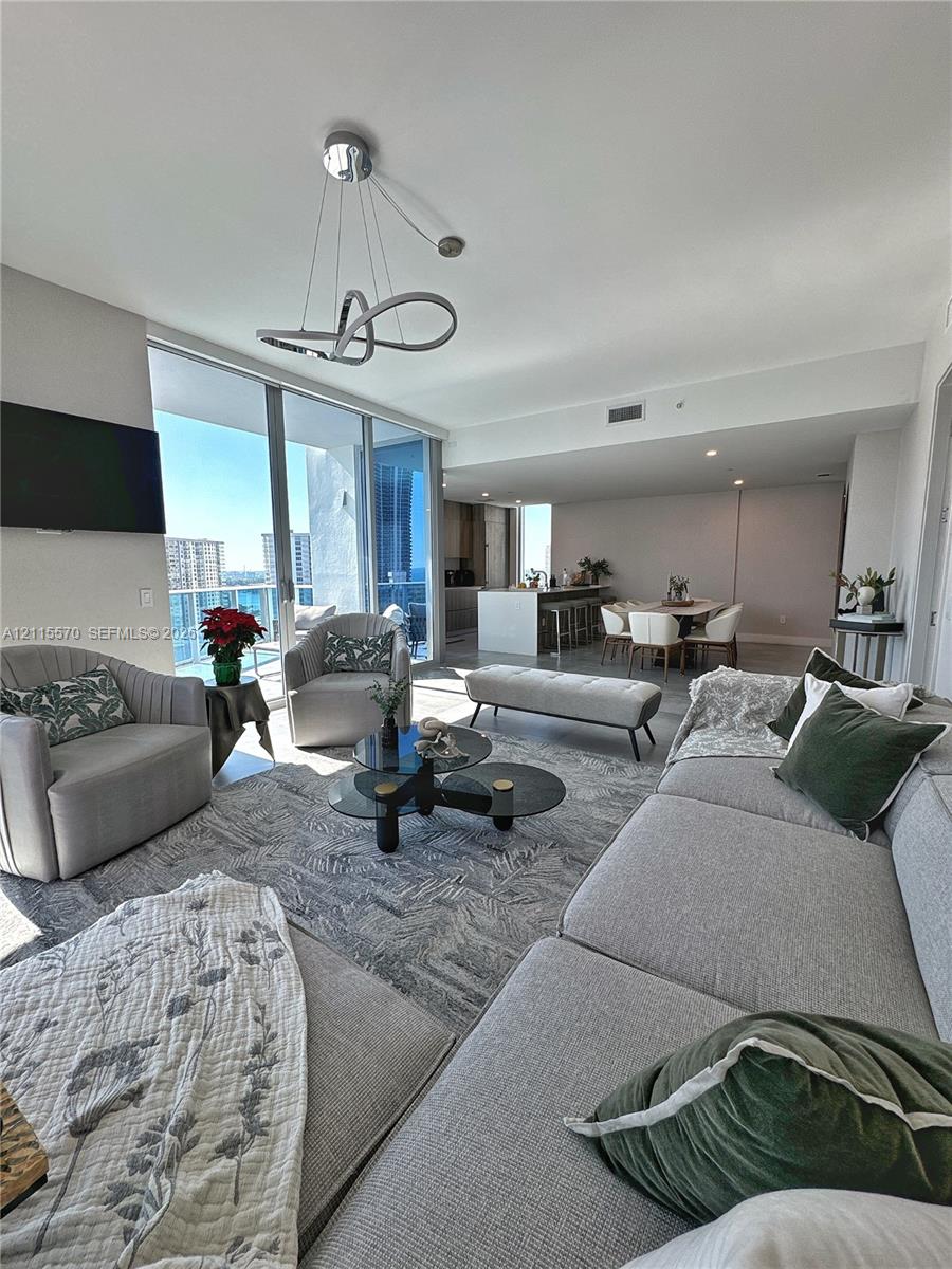 Open-concept living space featuring floor-to-ceiling glass sliding doors, modern brushed-metal sculptural chandelier, kitchen island with stone countertop, and neutral-toned flooring