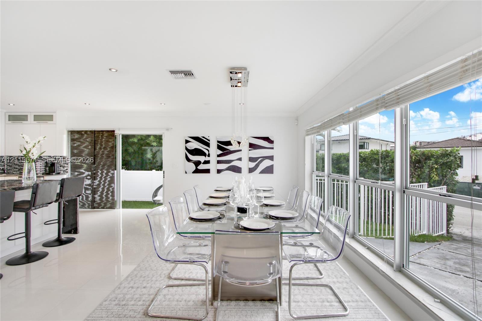 Open-concept dining area featuring large windows with natural lighting, polished tile flooring, recessed lighting, a modern pendant light fixture, and white cabinetry