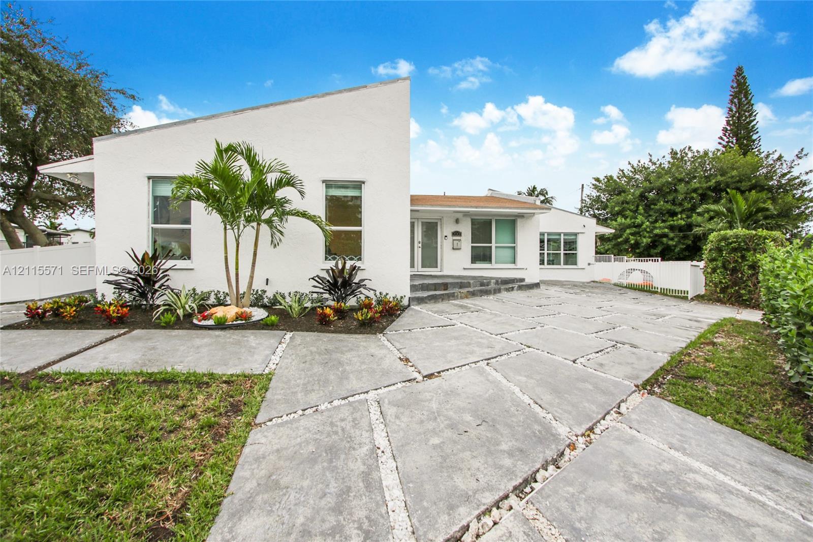 Modern architectural exterior featuring a geometric roofline, white stucco facade, large-format concrete paver driveway, integrated stone-accented entryway, and landscaped garden beds