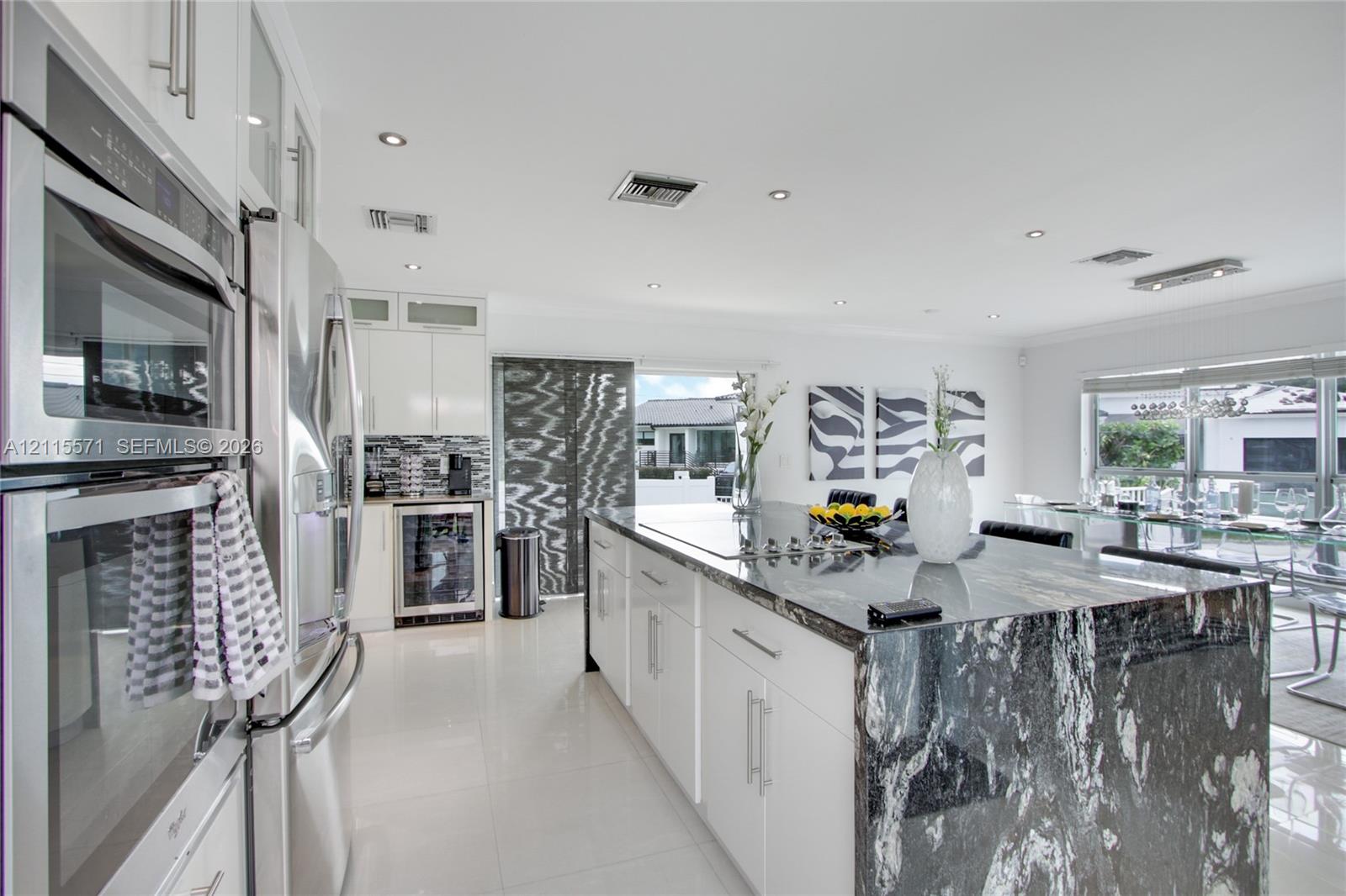 Kitchen featuring a center island with stone surfacing, stainless steel double wall ovens, stainless steel refrigerator, white cabinetry, and built-in under-counter beverage storage