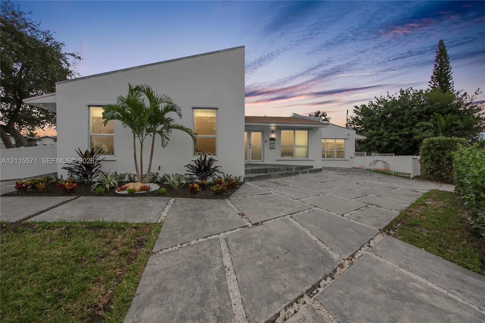 Mid-century modern exterior featuring a distinctive shed roofline, stucco facade, expansive concrete paver driveway with gravel accents, and manicured landscaping