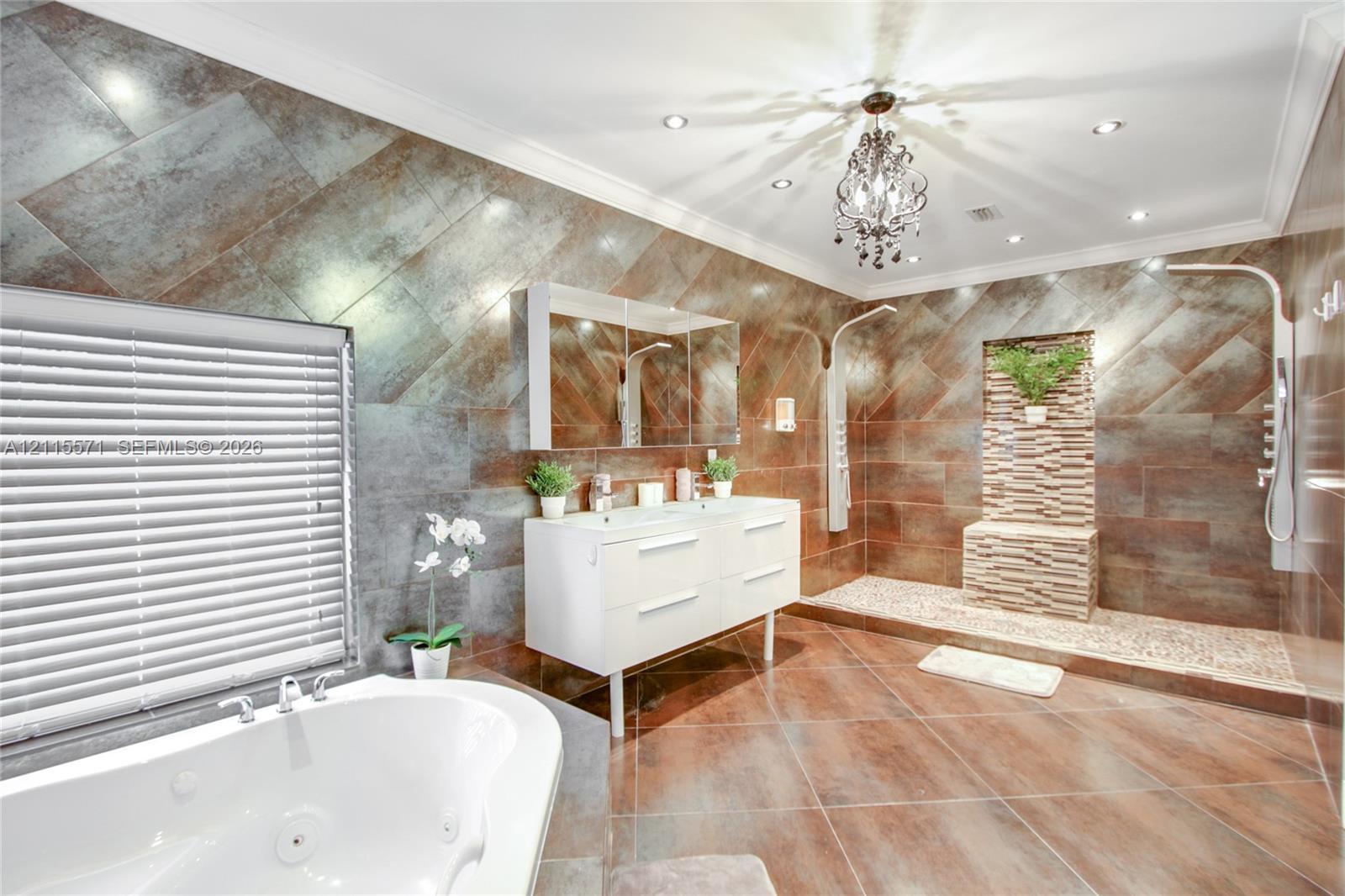Bathroom featuring large-format diagonal tile wall cladding, a double-basin floating vanity, a jetted soaking tub, a multi-head walk-in shower with pebble-stone flooring, and a crystal chandelier