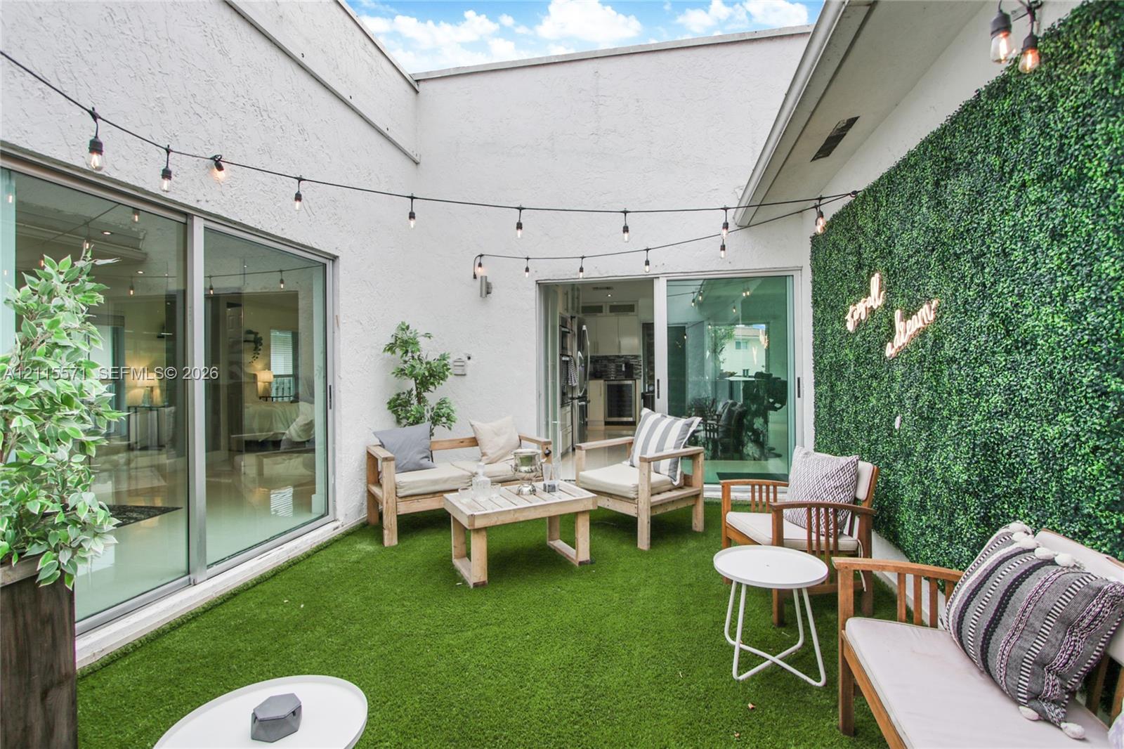 Private courtyard featuring high stucco walls, artificial turf, sliding glass doors, and a decorative greenery wall