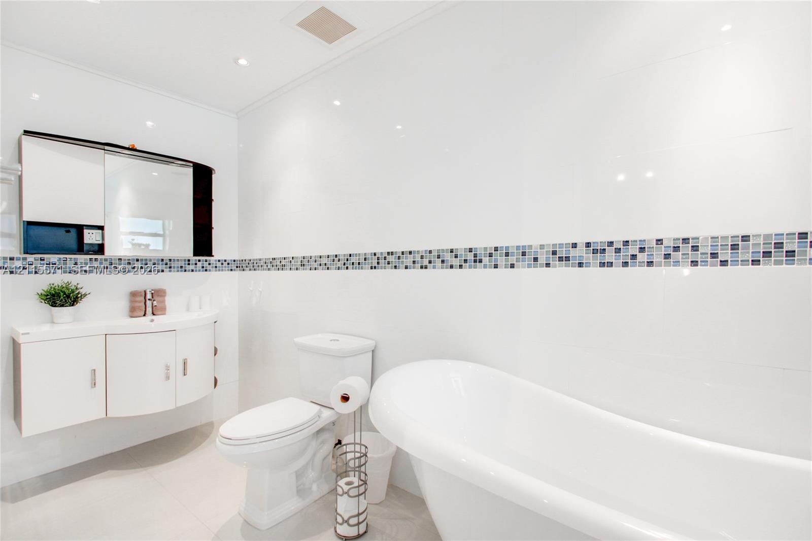 Freestanding soaking tub, wall-mounted curved vanity with integrated storage, built-in medicine cabinet, and decorative mosaic tile backsplash