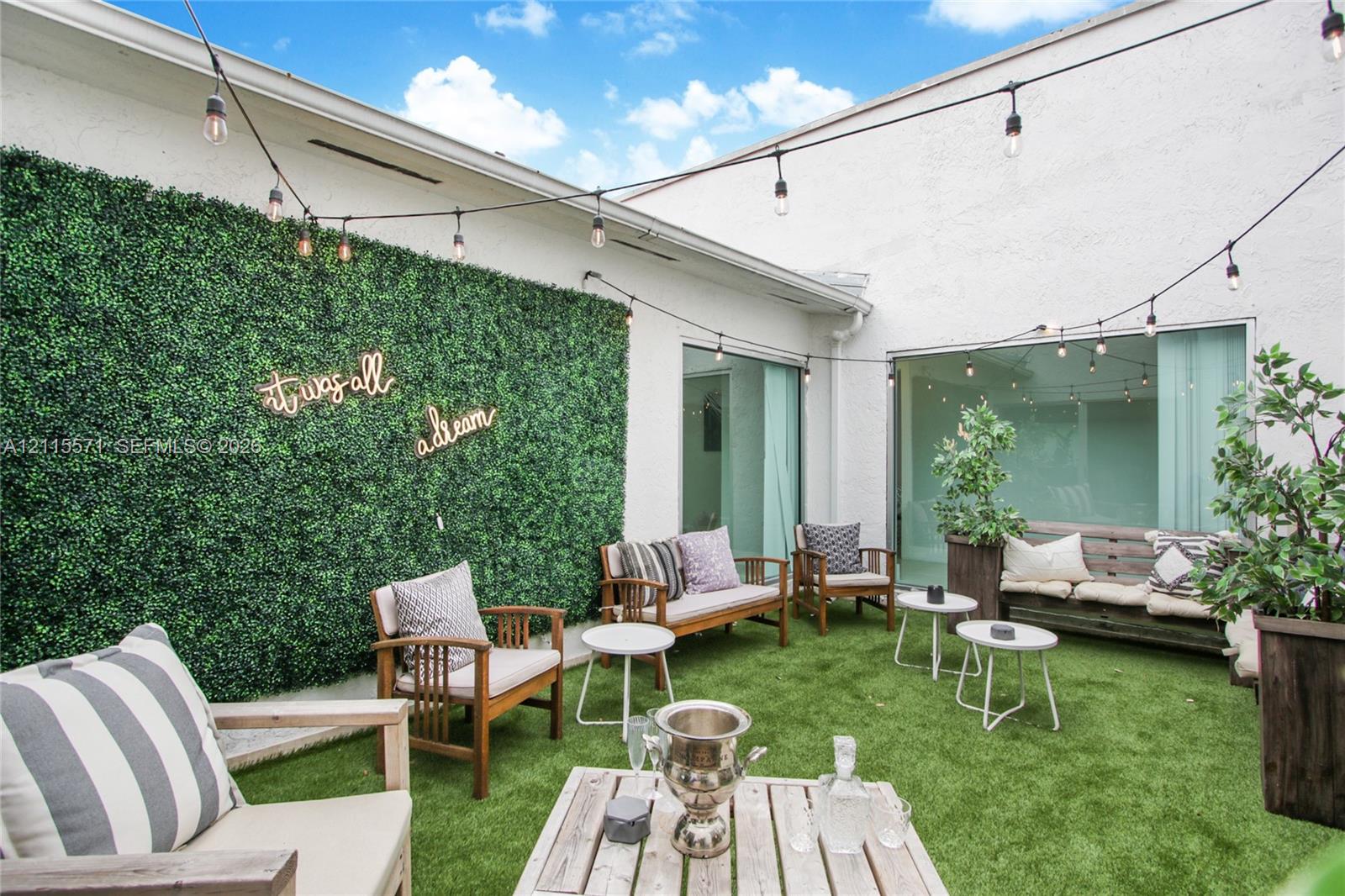 Private courtyard featuring synthetic turf, decorative greenery wall, and overhead string lighting