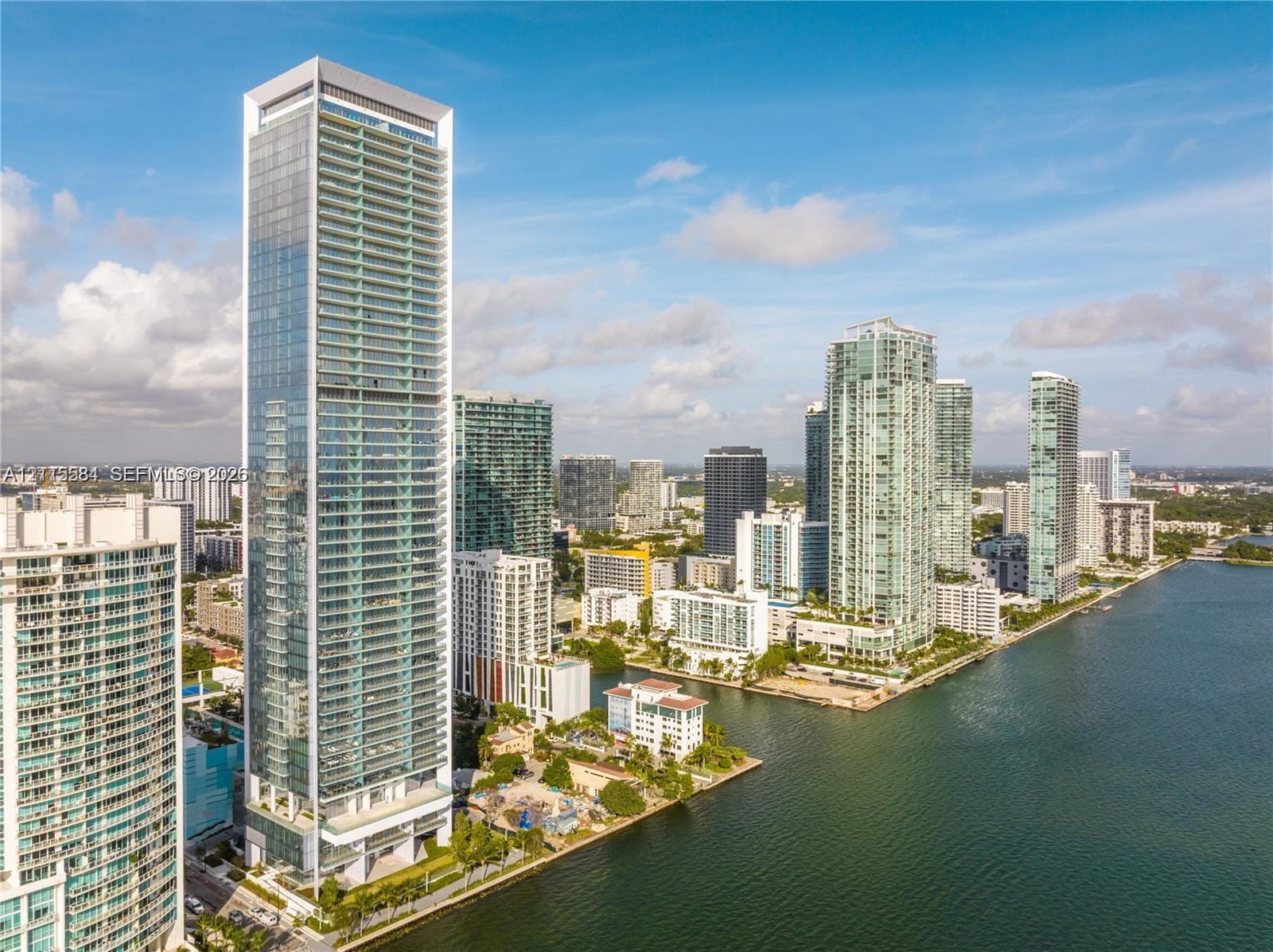 High-rise residential tower featuring a glass-curtain wall exterior, tiered architectural design, multiple private balconies, and a prominent waterfront location