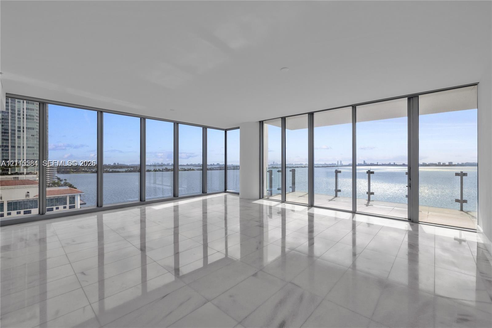 Floor-to-ceiling windows, wrap-around glass balcony railing, expansive stone tile flooring, and panoramic water exposure