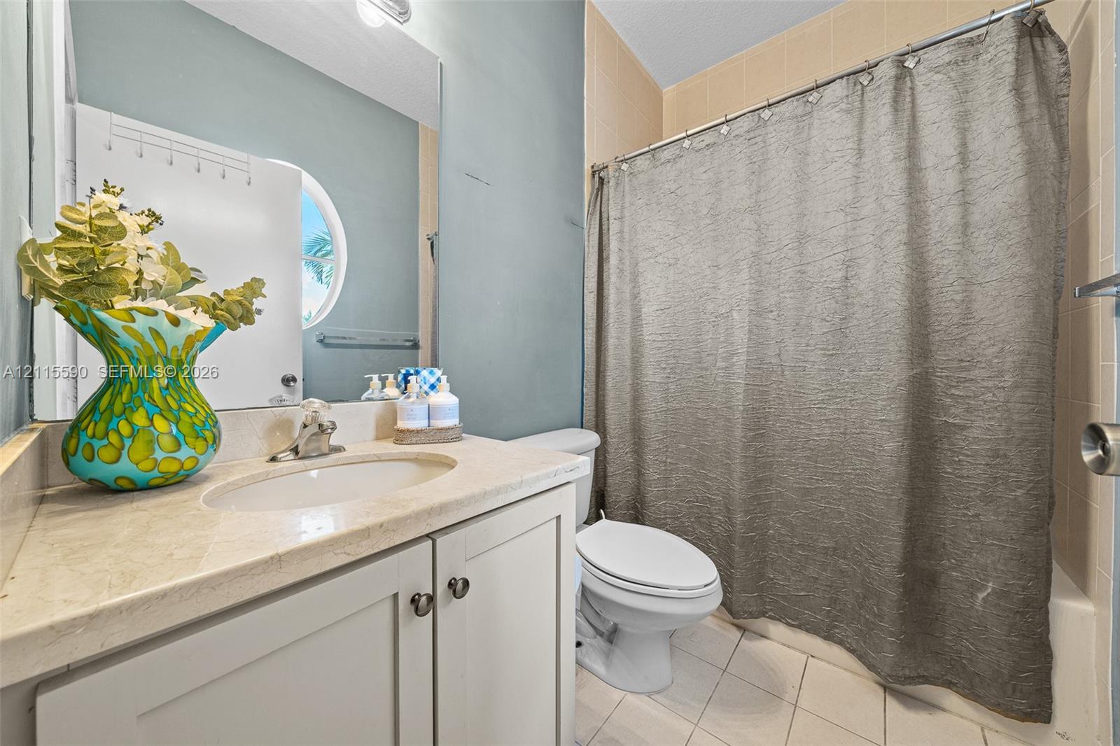 Bathroom featuring a vanity with a stone countertop, an integrated oval sink, a large wall-mounted mirror, a circular window, and tiled flooring