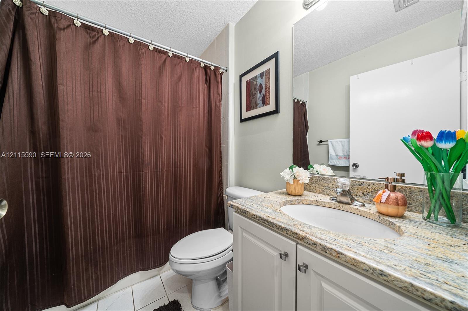 Bathroom featuring a vanity with stone countertop, integrated sink, white cabinetry, large wall-mounted mirror, and tile flooring