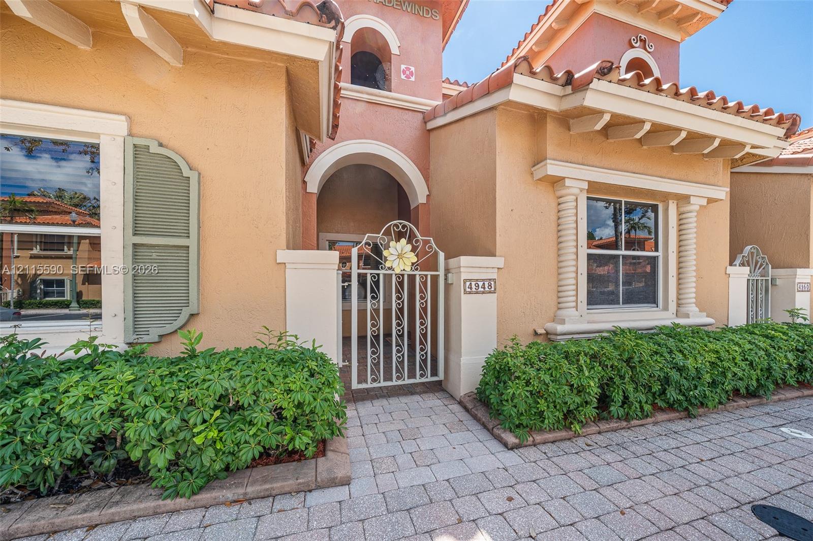 Stucco exterior featuring arched architectural detailing, decorative metal gate, pilasters, mission-style roof tiles, and paver walkway